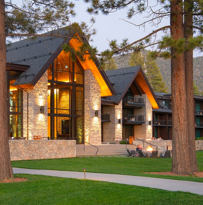 A luxury stone commercial building with large windows in front of a grassy lawn and pine trees